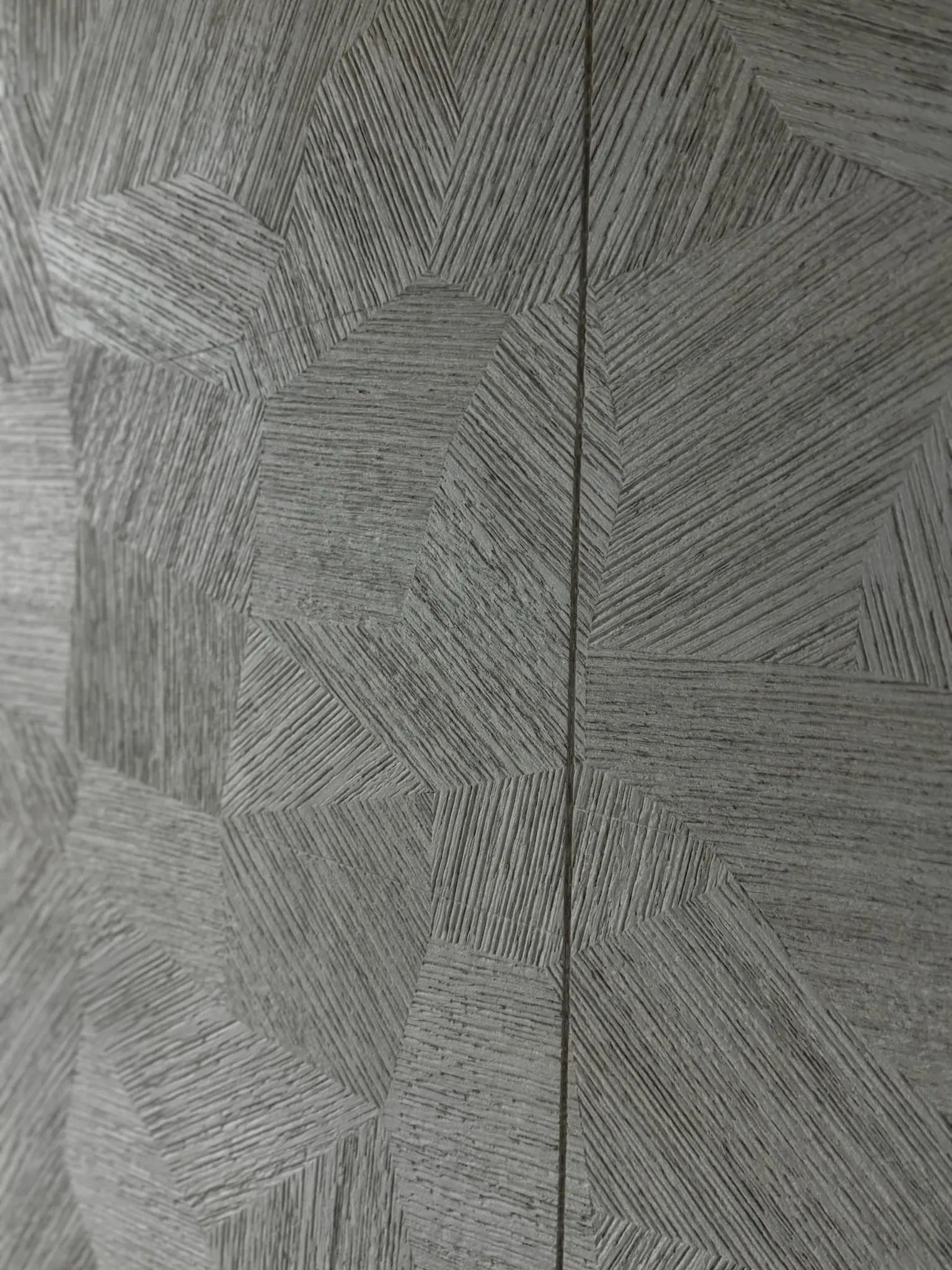 A grey timber panel carved in book-matched geometric facets, split by a hairline joint