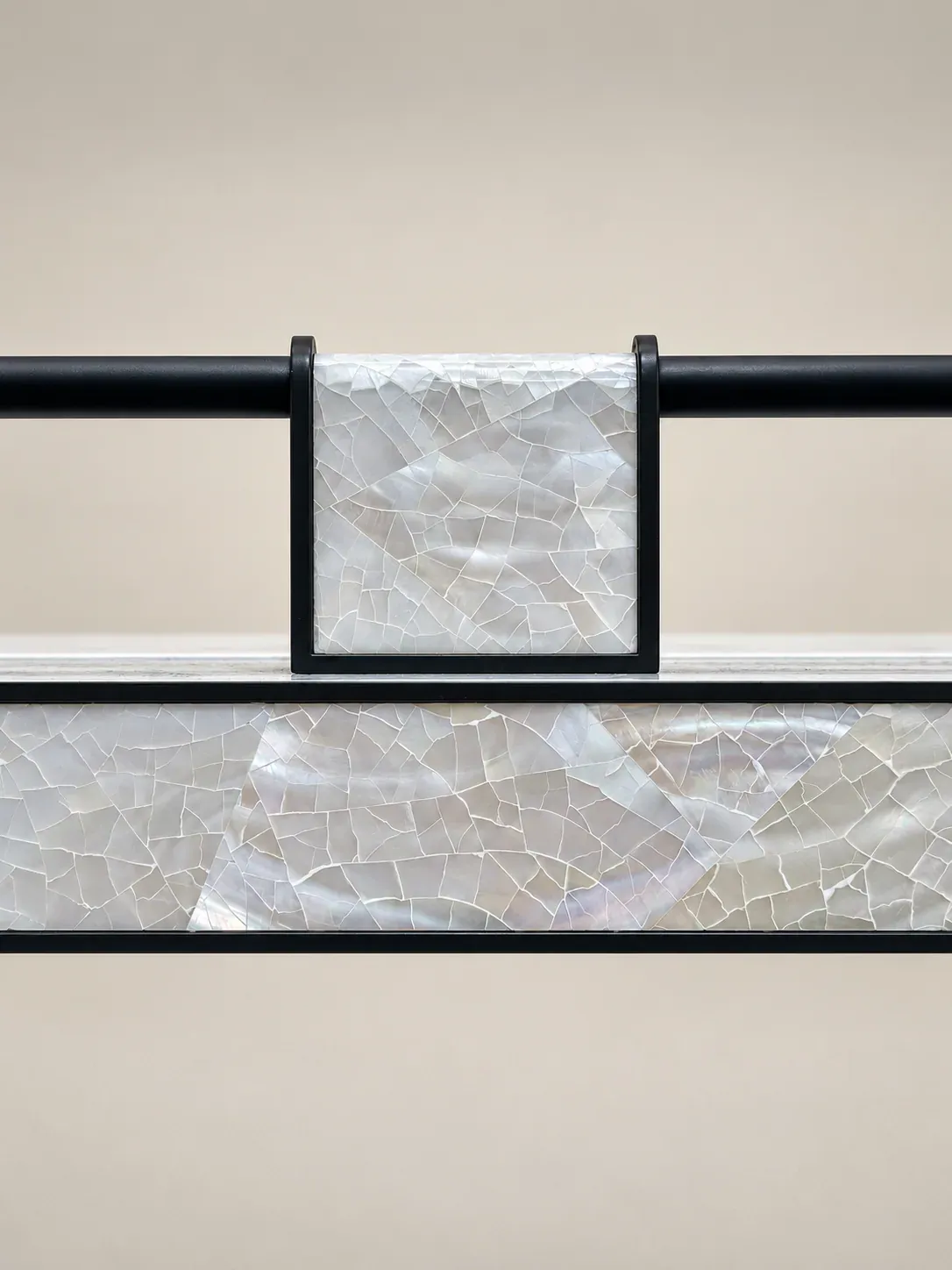 A mother-of-pearl inlay panel set between black metal rails, its tesserae catching the light